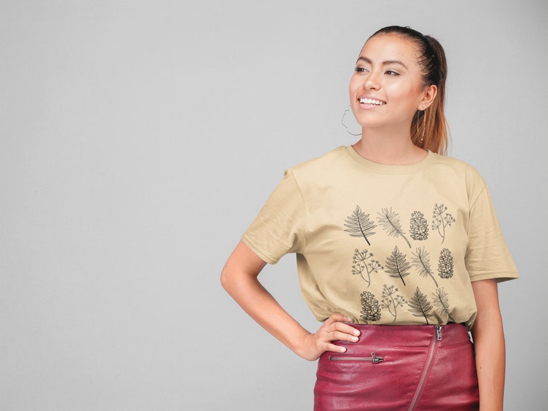 May include: A woman wearing a beige t-shirt with a black and white botanical print and a red leather skirt.