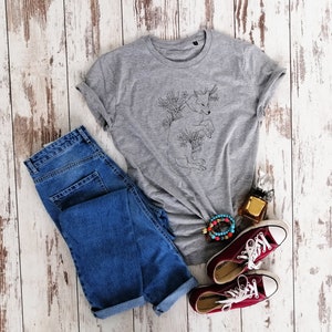 May include: A gray t-shirt with a black line drawing of a wolf surrounded by flowers. The shirt is paired with blue jeans, red converse shoes, and a beaded bracelet.