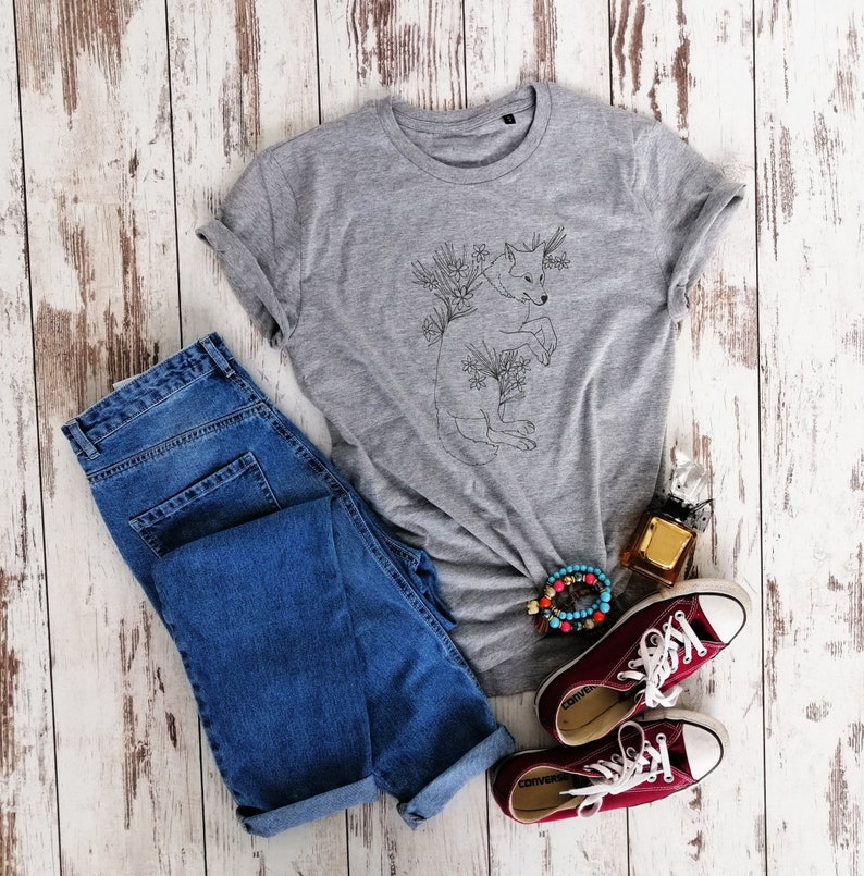 May include: A gray t-shirt with a black line drawing of a wolf surrounded by flowers. The shirt is paired with blue jeans, red converse shoes, and a beaded bracelet.