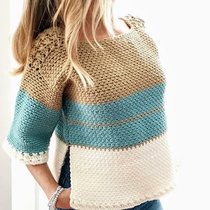Puede incluir: Un top de crochet con un diseño a rayas en beige, azul verdoso y blanco. El top tiene un corte holgado y mangas cortas.