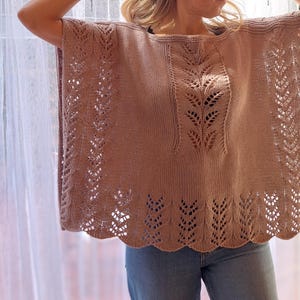 Puede incluir: Un poncho de tejido abierto en color marrón claro con intrincados diseños en forma de hojas. El poncho tiene un dobladillo festoneado y un diseño suelto y fluido. La prenda está hecha de un material de punto suave.