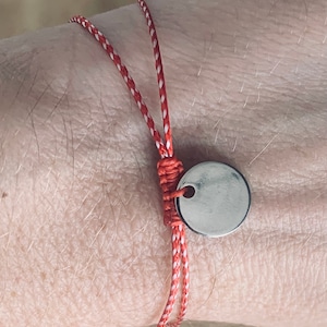 May include: Red and white braided cord bracelet with a silver round charm.