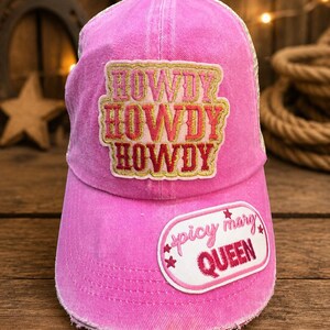 Puede incluir: Gorra de camionero rosa con la palabra "HOWDY" en un diseño apilado. La gorra también presenta un parche que dice "spicy mary QUEEN". La gorra tiene una parte trasera de malla.