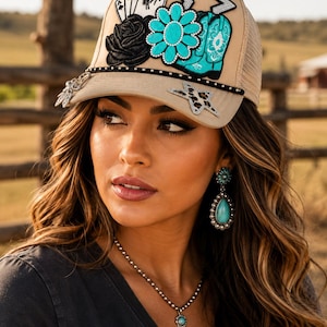 May include: A beige trucker hat featuring a variety of patches including three playing cards, a black rose, a turquoise flower, a turquoise cowboy boot, and two stars. The brim is accented with a black studded trim and a silver-toned charm.