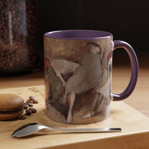 Puede incluir: Una taza de cerámica morada con una pintura de tres personas en grupo. La pintura es de estilo acuarela y presenta colores apagados de marrón, verde y blanco.