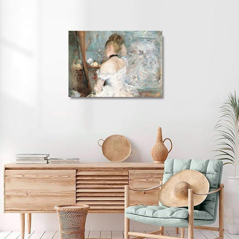 May include: A framed canvas print of a classic impressionist painting. The artwork depicts a woman in a white dress, viewed from the back, seated before a mirror. The color palette is soft, with blues, whites, and muted tones. The painting is displayed on a white wall.