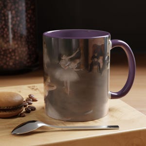 Puede incluir: Una taza de cerámica morada con asa blanca presenta una imagen vintage de una bailarina en un tutú blanco bailando en un escenario. La imagen está impresa en la parte delantera y trasera de la taza.
