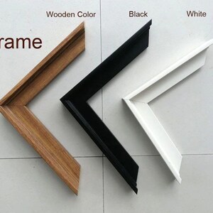 Puede incluir: Tres esquinas de marcos de fotos en diferentes colores: color madera, negro y blanco. La palabra "Frame" está escrita en la esquina superior izquierda. Los marcos están en ángulo, mostrando las uniones de las esquinas.