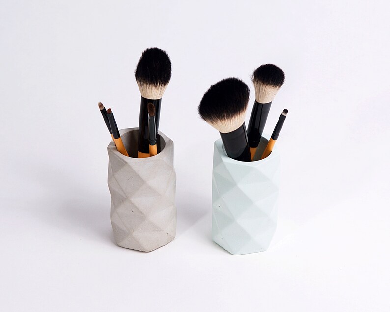 May include: Two geometric concrete makeup brush holders, one gray and one light blue, each filled with makeup brushes.