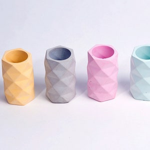 May include: Four geometric concrete planters in different colours: yellow, grey, pink, and light blue. The planters are all the same size and shape, with a hexagonal base and a cylindrical body.