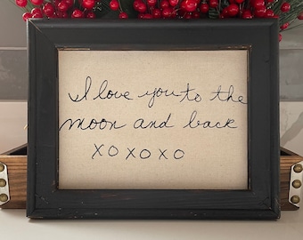 Puede incluir: Un lienzo enmarcado en negro con el mensaje escrito a mano "I love you to the moon and back xoxo" en tinta negra.