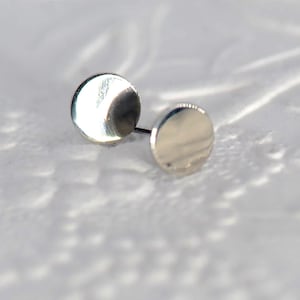 May include: A pair of silver stud earrings with a circular design. The earrings are small and simple, making them a versatile accessory.