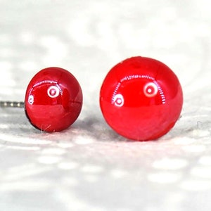 May include: A pair of red glass stud earrings. The earrings are round and have a glossy finish.