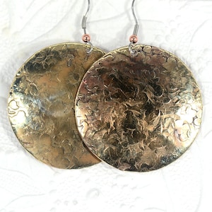 以下が含まれることがあります： テクスチャ加工された花柄の大きな丸い金色のイヤリングのペア。イヤリングは真鍮製で、ハンマー仕上げが施されています。