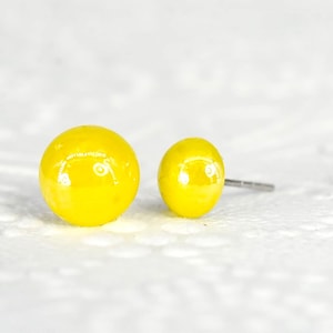 May include: A pair of yellow round stud earrings. The earrings are made of a shiny, smooth material.