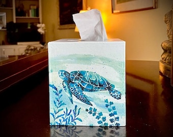 May include: A white tissue box cover with a watercolour design of a sea turtle swimming in blue and green water with seaweed.