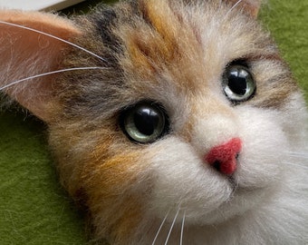 May include: Close-up of a calico cat's face. The cat has green eyes, a pink nose, and white fur with patches of brown and orange.