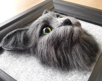 May include: A close-up of a gray felt cat head with green eyes, framed in a black wood frame.