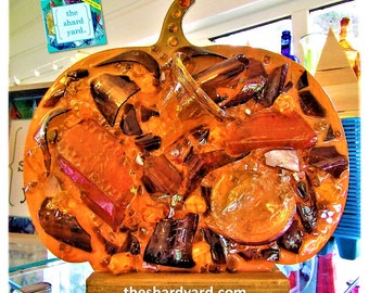 Peut inclure: Sculpture en résine orange en forme de citrouille avec une tige en verre et remplie de tessons de verre colorés. La sculpture est sur un socle en bois et porte le texte "the shard yard" sur le socle.