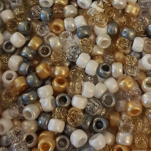 Puede incluir: Primer plano de una colección de cuentas de varios colores y texturas. Las cuentas incluyen blanco, dorado, plateado y transparente, algunas con un acabado nacarado o brillante. Las cuentas son cilíndricas y parecen ser de plástico o vidrio.