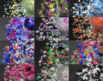 May include: Assortment of butterfly-shaped glitter in various colors, including green, blue, purple, and red, displayed in small, clear plastic jars. The glitter has a reflective, iridescent finish, creating a shimmering effect. Ideal for nail art or craft projects.