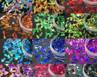 May include: Assortment of colorful, tree-shaped glitter in small, clear plastic containers. The glitter colors include shades of red, green, blue, purple, gold, and silver. Ideal for crafts, nail art, or festive decorations.