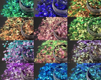May include: A collection of small, butterfly-shaped glitter in various colors, including green, blue, gold, and purple. The glitter is contained in small, clear plastic jars, arranged in a grid pattern. The glitter is likely used for crafts or nail art.