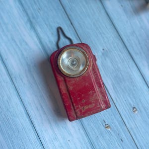 Peut inclure: Une lampe torche vintage rouge avec un boîtier en métal et une lentille ronde. La lampe torche a une poignée noire et le mot "WONDER" est imprimé sur le côté.