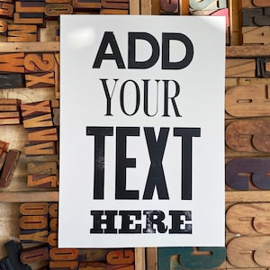 May include: A white poster with black text that reads "ADD YOUR TEXT HERE" against a background of wooden letterpress blocks.