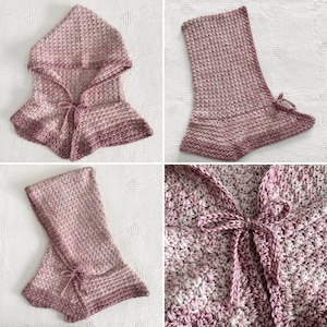 May include: A pink and white crocheted hooded scarf with a tie closure. The scarf is made with a textured stitch and has a gradient colour pattern.