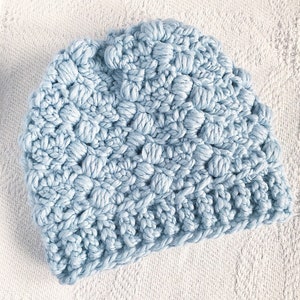 May include: A light blue crocheted beanie hat with a textured, puffy design.