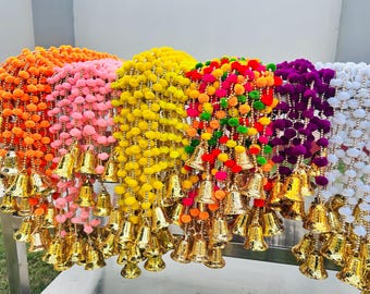 Può includere: Una ghirlanda colorata di pompon con campanelle dorate appese a ogni filo. La ghirlanda è realizzata in vari colori, tra cui arancione, rosa, giallo, rosso, verde, viola e bianco.