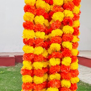 K&ouml;nnte beinhalten: Eine Girlande aus k&uuml;nstlichen Ringelblumen in Gelb und Orange. Die Girlande ist aus Papier und zu einem langen Strang zusammengef&uuml;gt.