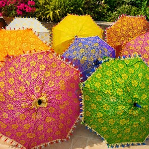 Könnte beinhalten: Eine Sammlung lebendiger Sonnenschirme mit komplizierten goldenen Blumenmustern auf farbenfrohen Stoffhintergründen in Pink, Grün, Orange, Gelb und Blau. Jeder Sonnenschirm ist mit einer dekorativen Fransenborte an den Rändern versehen.