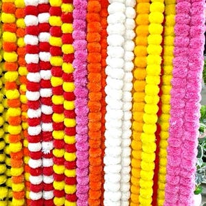 Könnte beinhalten: Eine lebendige Präsentation farbenfroher Blumengirlanden. Die Girlanden sind vertikal angeordnet und zeigen eine Vielzahl von Farben, darunter Gelb, Orange, Rosa, Rot und Weiß. Die Blumen scheinen dicht gepackt zu sein und erzeugen eine strukturierte Anordnung.