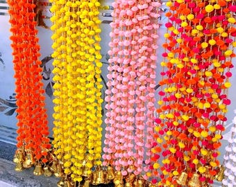 May include: A set of five colourful garlands with pom-poms and gold bells. The garlands are orange, yellow, pink, red, and white.