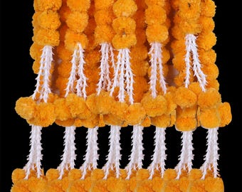 Può includere: Una ghirlanda di pompon di fiori di calendula arancioni brillanti con accenti di corda bianca. La ghirlanda è composta da più fili di fiori.