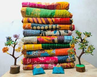 May include: A stack of colorful, patchwork quilts with various patterns and colors, including pink, green, yellow, and orange. The quilts are neatly folded and stacked. Decorative miniature trees and blue fabric pyramids are in the foreground.