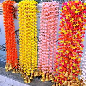 May include: A display of colorful, decorative garlands. The garlands are made of small, round, pom-pom-like elements in shades of orange, yellow, pink, and red. Each strand is adorned with gold-colored bells at the bottom, creating a festive and vibrant appearance.