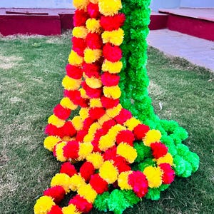 K&ouml;nnte beinhalten: Eine Girlande aus roten und gelben Kunstblumen, mit einer gr&uuml;nen Girlande im Hintergrund. Die Girlanden bestehen aus Pompons und sind vertikal angeordnet.