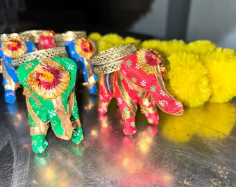 Puede incluir: Cuatro pequeñas figuritas de elefante decorativas hechas de tela. Los elefantes son de color rojo, verde y azul con detalles dorados. Los elefantes están sentados sobre una superficie plateada.