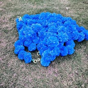 K&ouml;nnte beinhalten: Eine Girlande aus blauen k&uuml;nstlichen Blumen aus Papier, mit einem gr&uuml;nen Draht, der durch die Mitte verl&auml;uft. Die Girlanden liegen auf einem Bett aus gr&uuml;nem Gras.