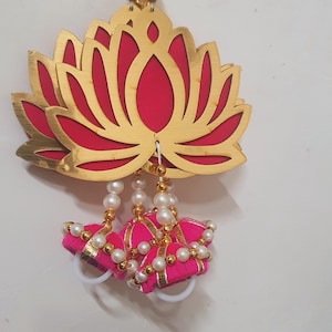 May include: A pink and gold lotus flower ornament with a string of white pearls and pink tassels hanging from it.