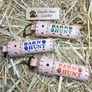 May include: Three leather keychains with the words "Barn Hunt" and paw prints in different colors. The keychains are made by Double Dew Leather.