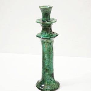 Puede incluir: Un candelero de cerámica verde con un diseño de varios niveles. El candelero tiene una base alta y delgada y una parte superior ancha y plana.