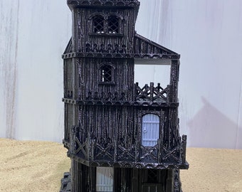 May include: A black miniature house with a detailed design, featuring multiple levels, windows, and a small balcony. The house has a textured, weathered appearance, with a light grey door and a rocky base. The design evokes a gothic or fantasy theme.