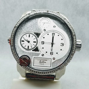 May include: A silver Techno Pav&eacute; watch with a silver band and a white face. The watch has three sub-dials, two of which are round and one of which is rectangular. The watch face is covered in a sparkly silver material.