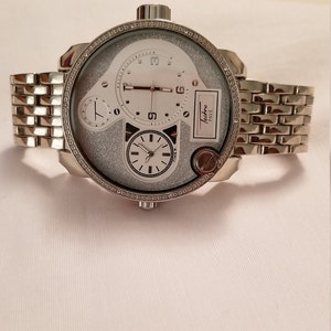 May include: A silver Techno Pave watch with a white face and a silver band. The watch has a glittery face and multiple hands.