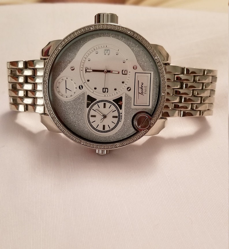 May include: A silver Techno Pave watch with a white face and a silver band. The watch has a glittery face and multiple hands.