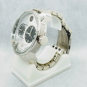 May include: A silver wristwatch with a multi-layered dial and a silver metal band. The watch is on a white display stand.